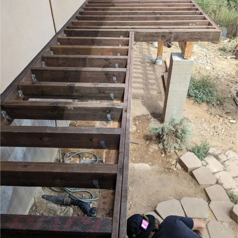 A man is working on a wooden deck in the dirt