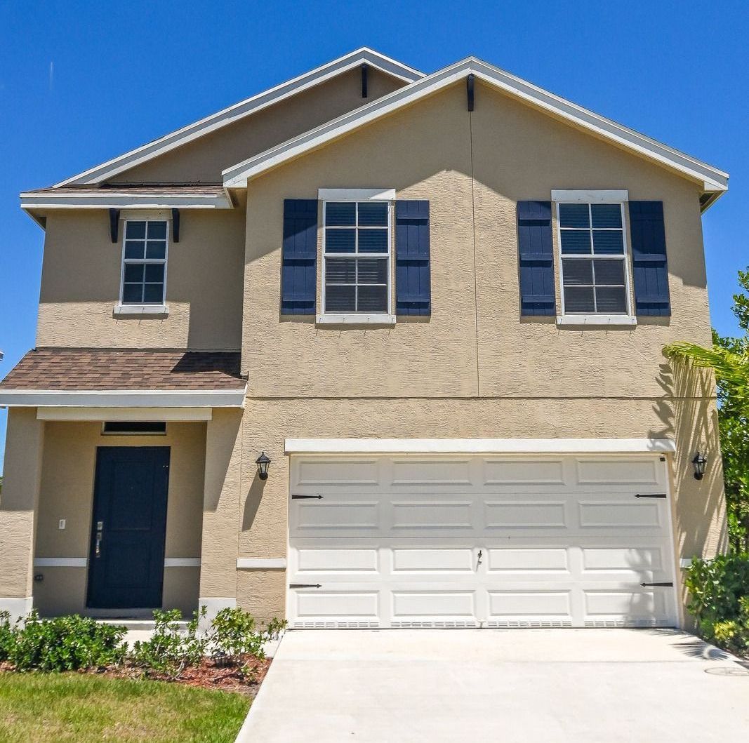 A tan house with white garage doors and black shutters