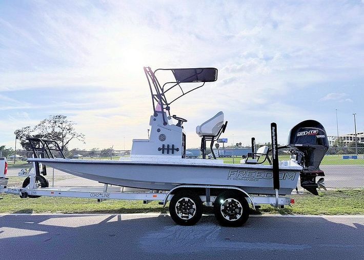 New 2026 Freedom Commander shallow water fishing boat on a trailer by the road at sunset, with radar and motor mounted.
