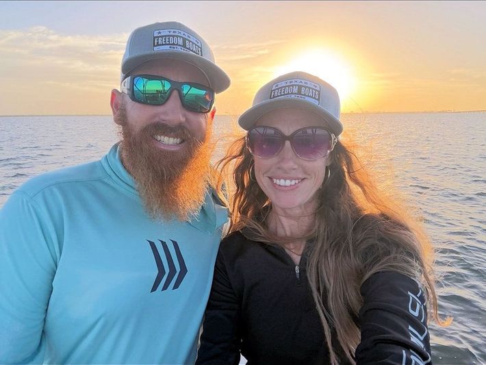 Smiling couple in hats and sunglasses taking a selfie on a boat at sunset