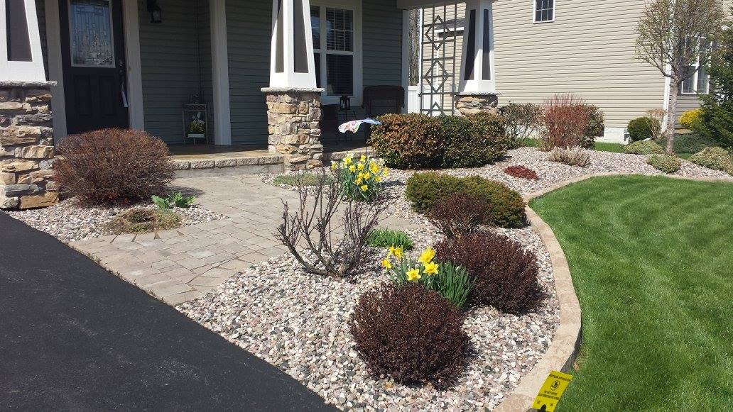 House front with stone pillars, gravel landscaping, blooming daffodils, and a curved lawn.