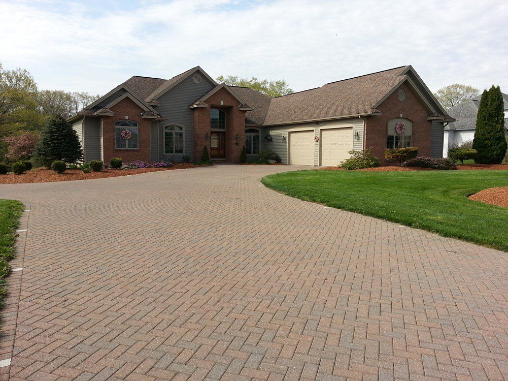 House with brick and gray siding, arched driveway, two-car garage, and landscaped lawn.
