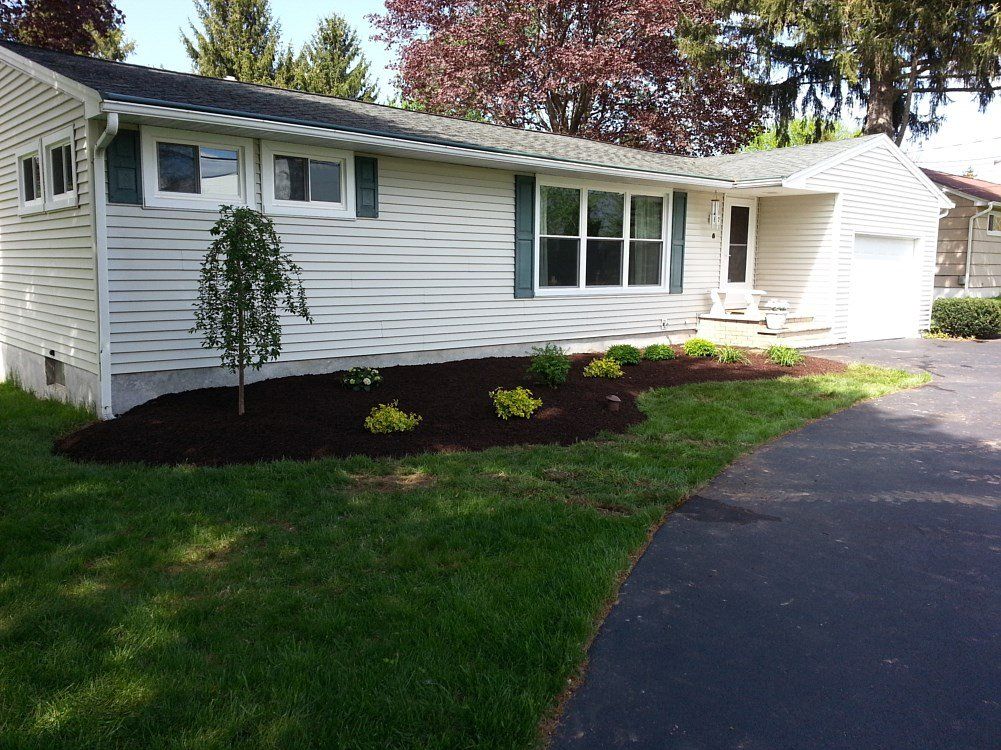 White house with green shutters, a new mulch bed, and a driveway on a sunny day.