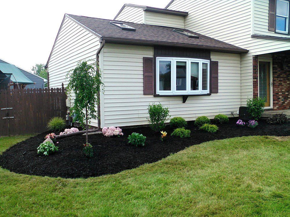 House with landscaped flower bed and dark mulch, green lawn.