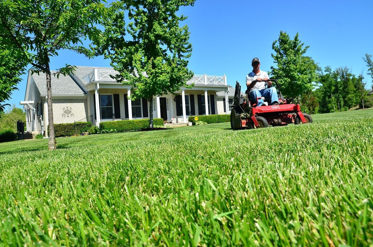 Man mowing lawn with red riding mower in front of a house on a sunny day.