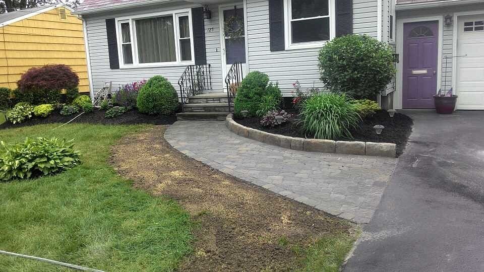 House with a paved walkway, flowerbeds with dark mulch, and a purple front door.