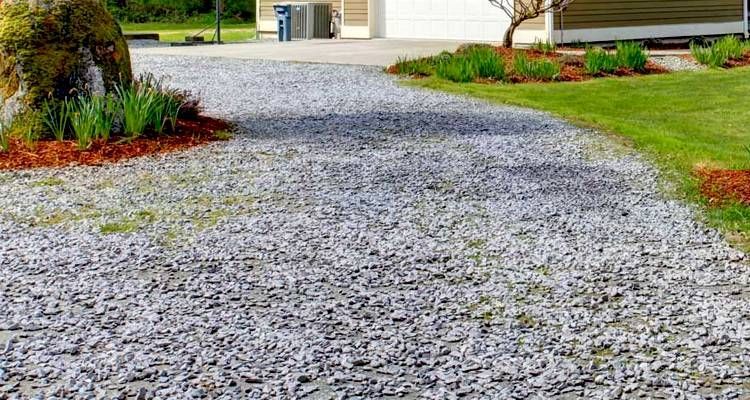 Gravel driveway leading to a garage, bordered by grass and mulch with a large rock on the left.