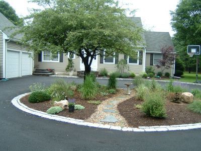 A house with a circular driveway and landscaped island with stone path, and a basketball hoop.