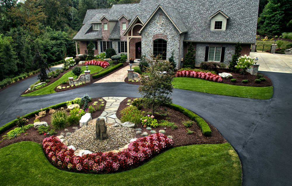Stone house with landscaped lawn and curving driveway with flower beds.