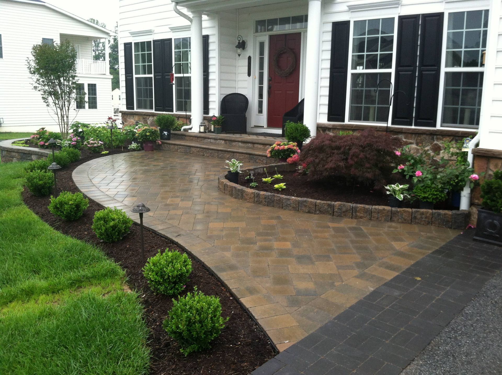 Well-landscaped home entrance with curved brick pathway, shrubs, and flower beds.