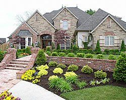 Brick and stone house with landscaped front yard, including bushes, flowers, and a brick walkway.