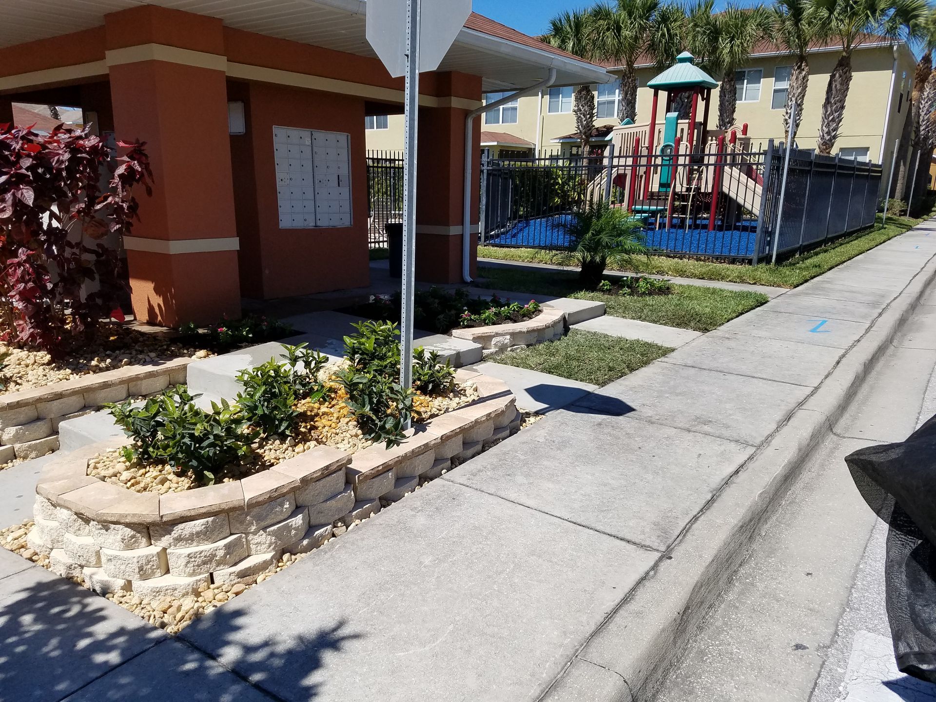 A sidewalk leads to a stone planter bed in front of a community mail station with a nearby playground in the background.