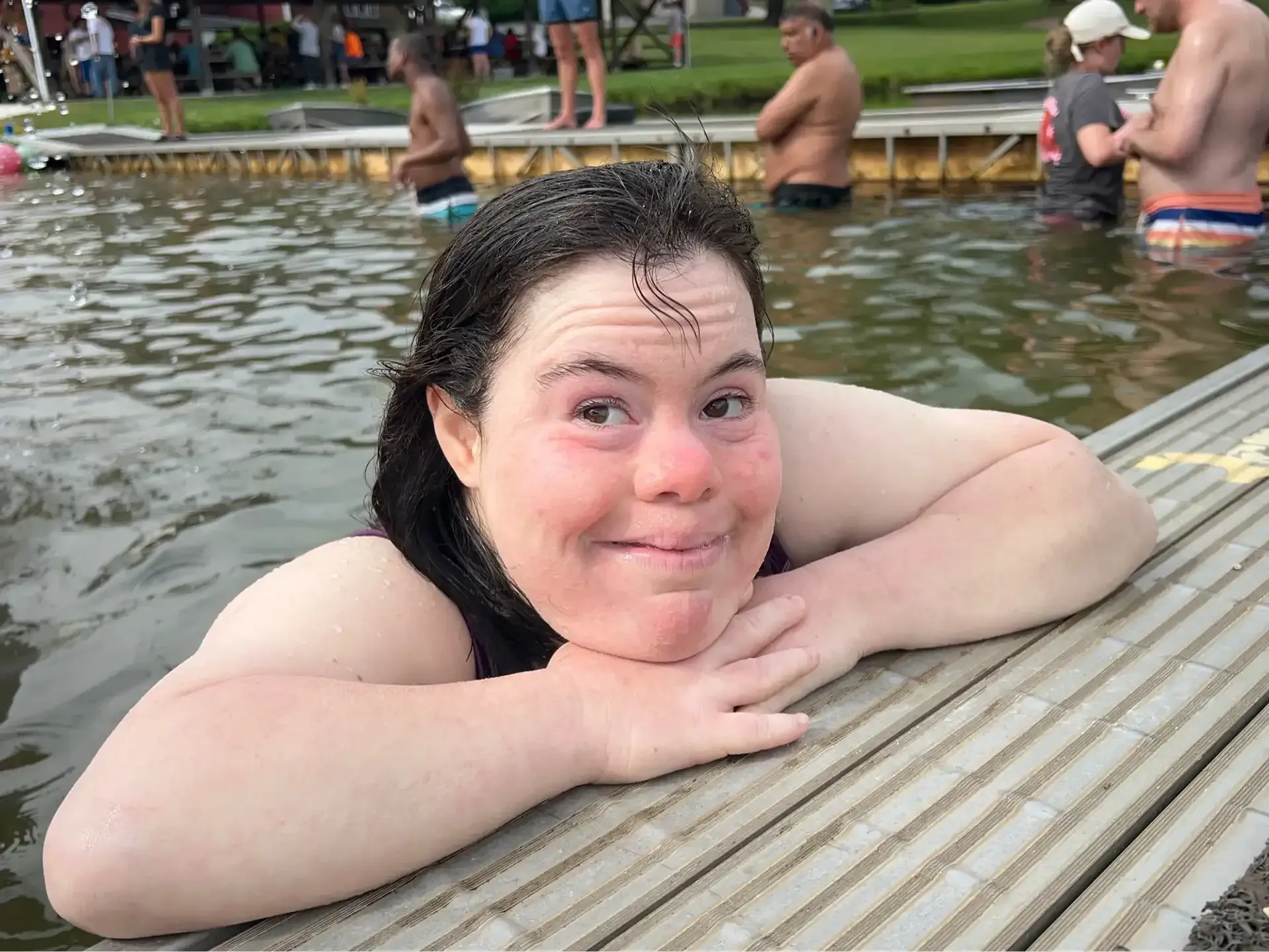 Woman in water, smiling, resting on a wooden dock at Camp Jaycee