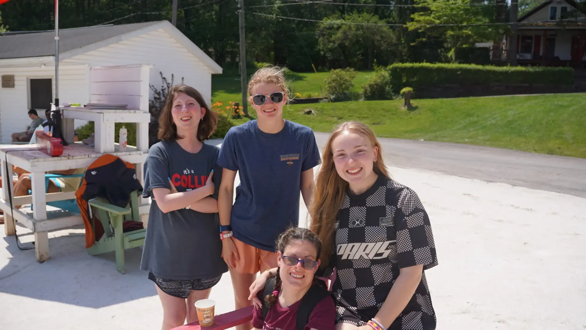 Four smiling people pose outdoors, near a small building with a wooden structure. Sunny day in the Poconos