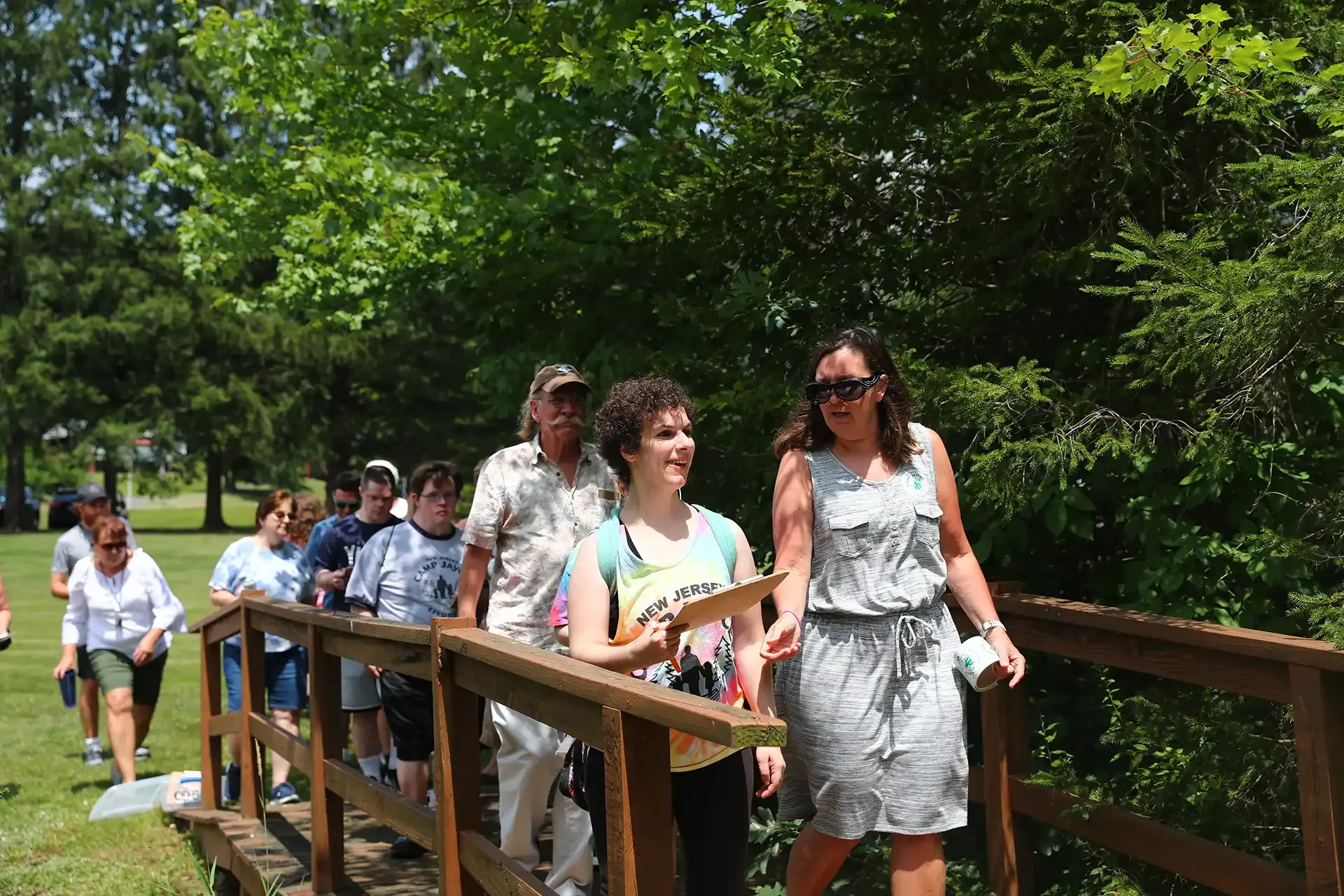 People walking across a wooden bridge in a park on a sunny day.