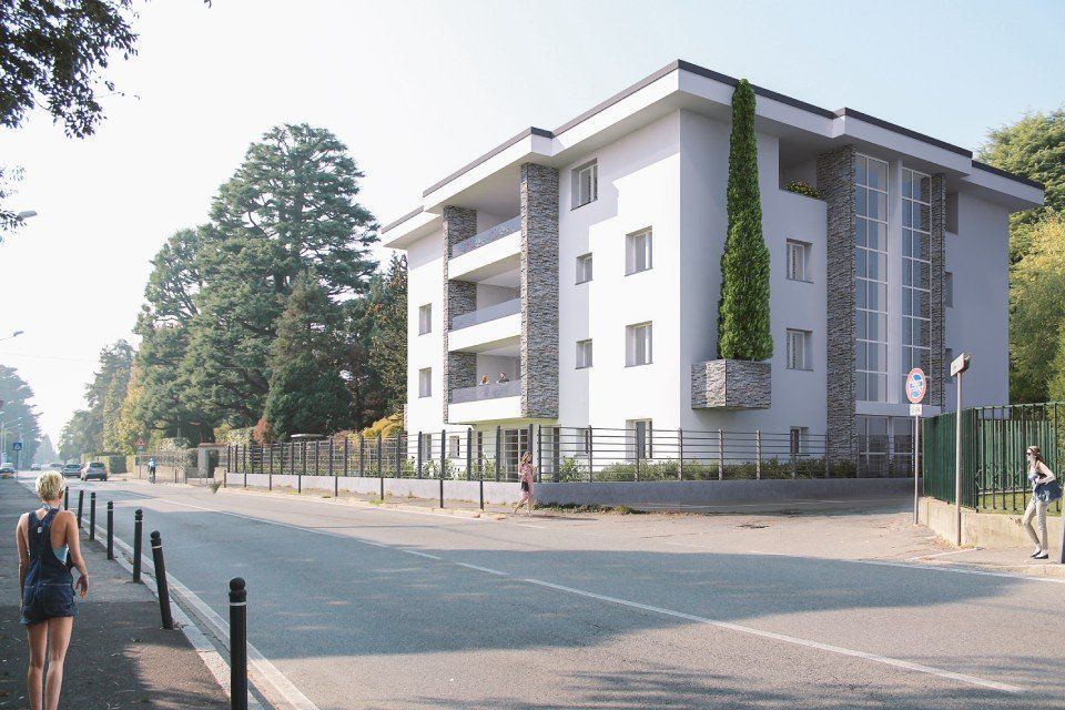 Un moderno edificio residenziale bianco con angoli impreziositi da dettagli in pietra sorge lungo una strada, fiancheggiato da alberi e pedoni.