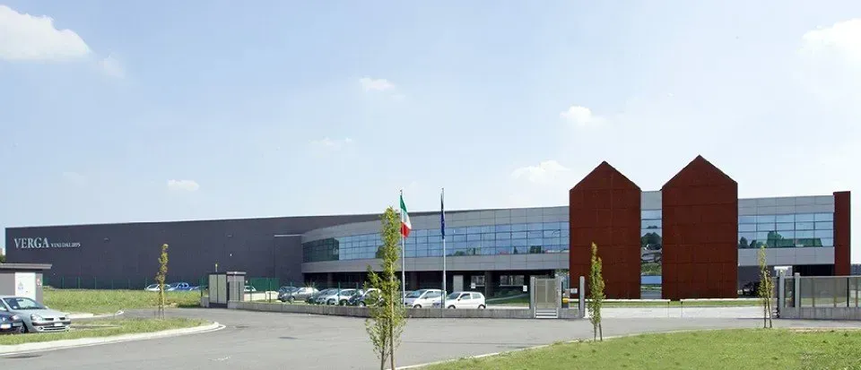 Moderno edificio industriale caratterizzato da una lunga parete grigia, facciata in vetro e due imponenti strutture a punta in mattoni color ruggine.