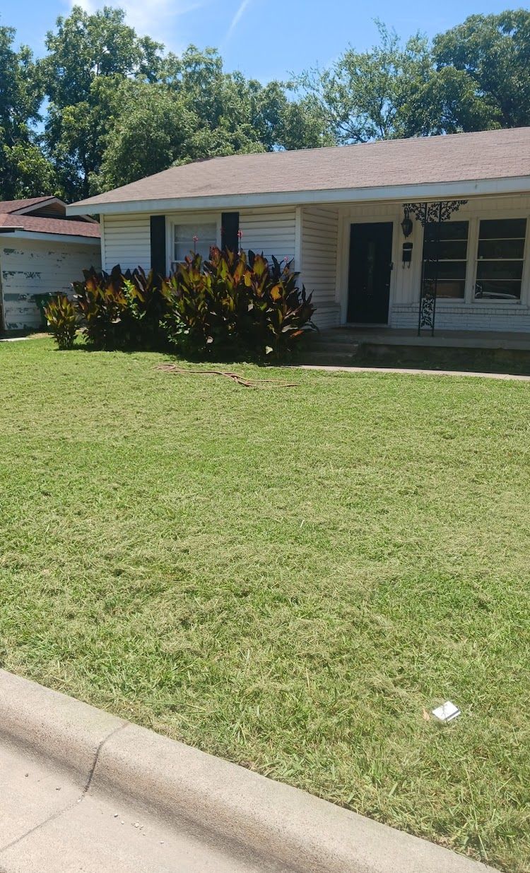 White house with dark door, front yard with grass, bushes, and a sidewalk.