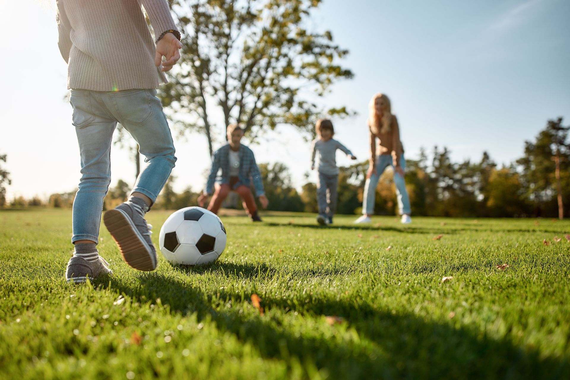 Group of children playing soccer on green grass with a blue sky in the background