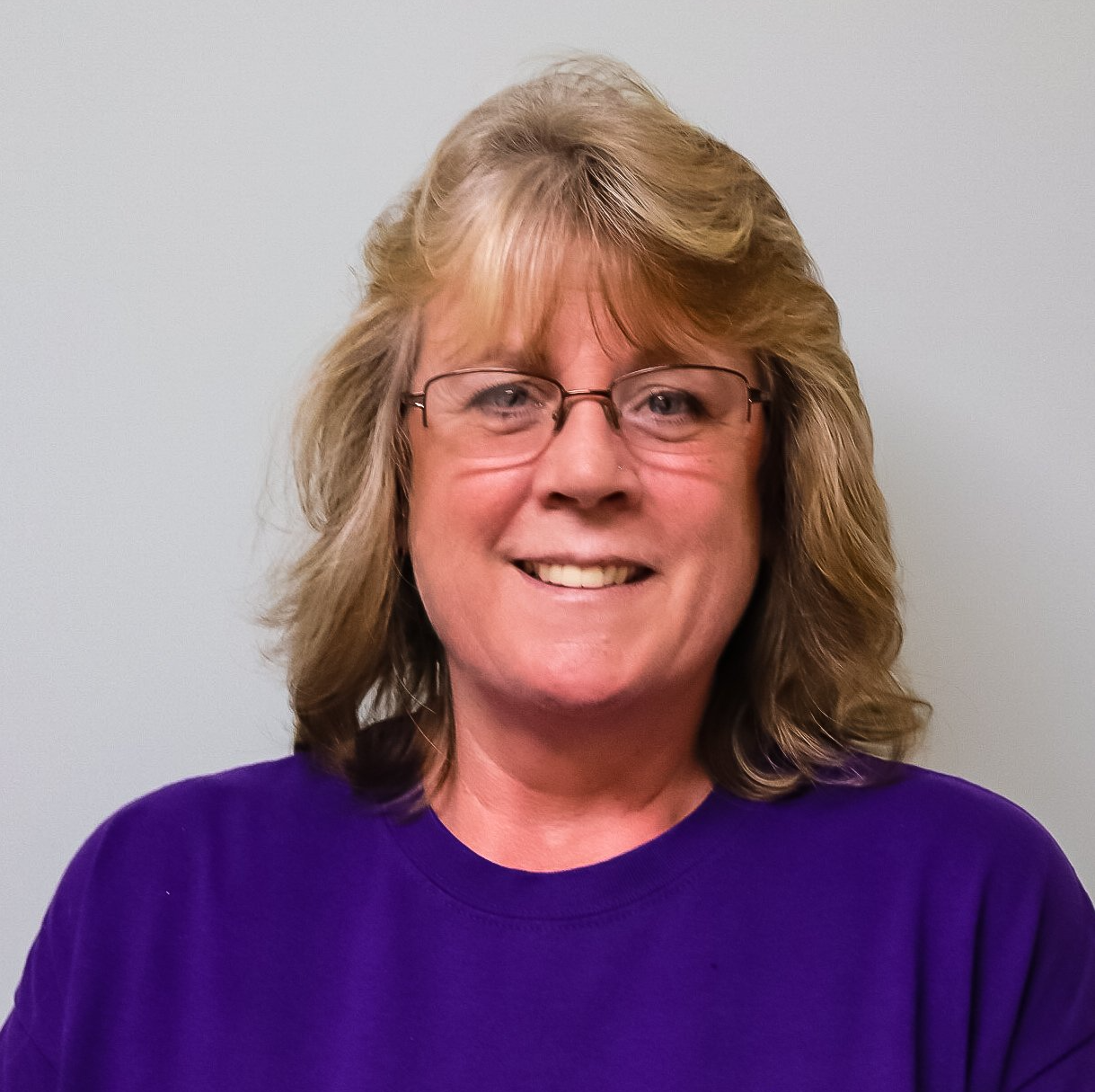 Smiling woman with glasses in a purple shirt against a light gray background