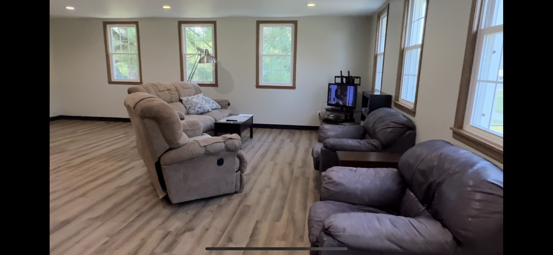 Spacious living room with brown leather recliners, wood flooring, and large windows.