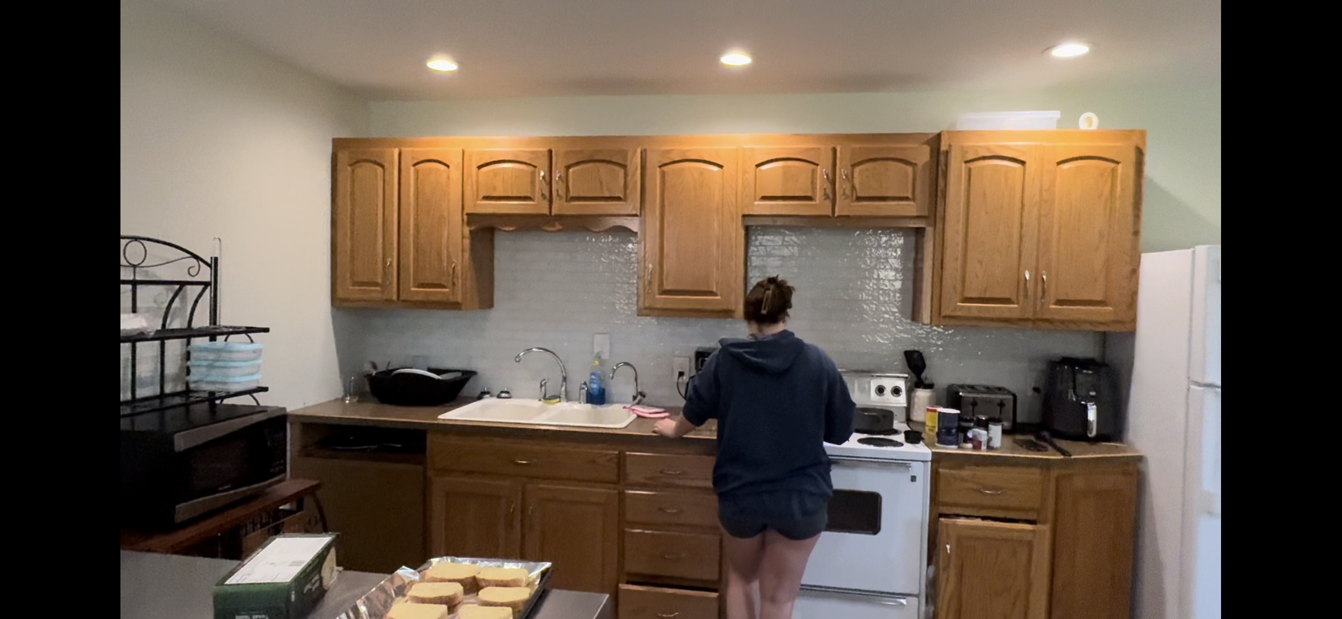 Person standing at a kitchen counter in front of wooden cabinets and a white stove.