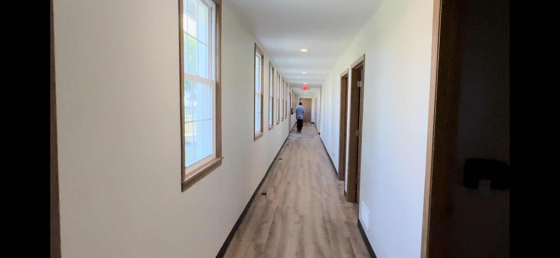 Long hallway with wood floors, white walls, windows on the left, and doors along the right