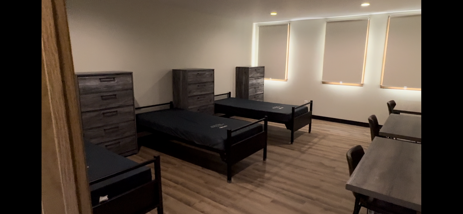 Sparse bedroom with two single beds, dresser, and vanity along a wood floor wall with windows.