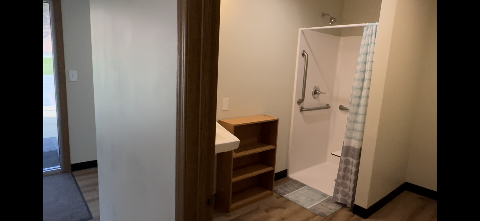 Bathroom vanity and shower area with tan tile and a striped shower curtain in a doorway.