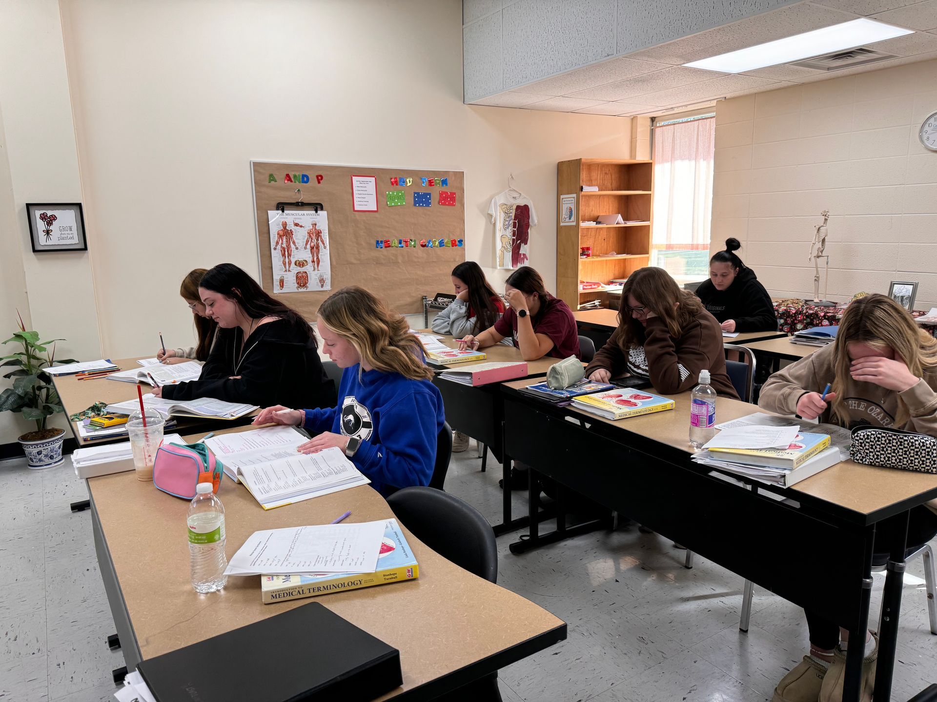 Students working quietly at desks in a classroom, writing on papers and notebooks.