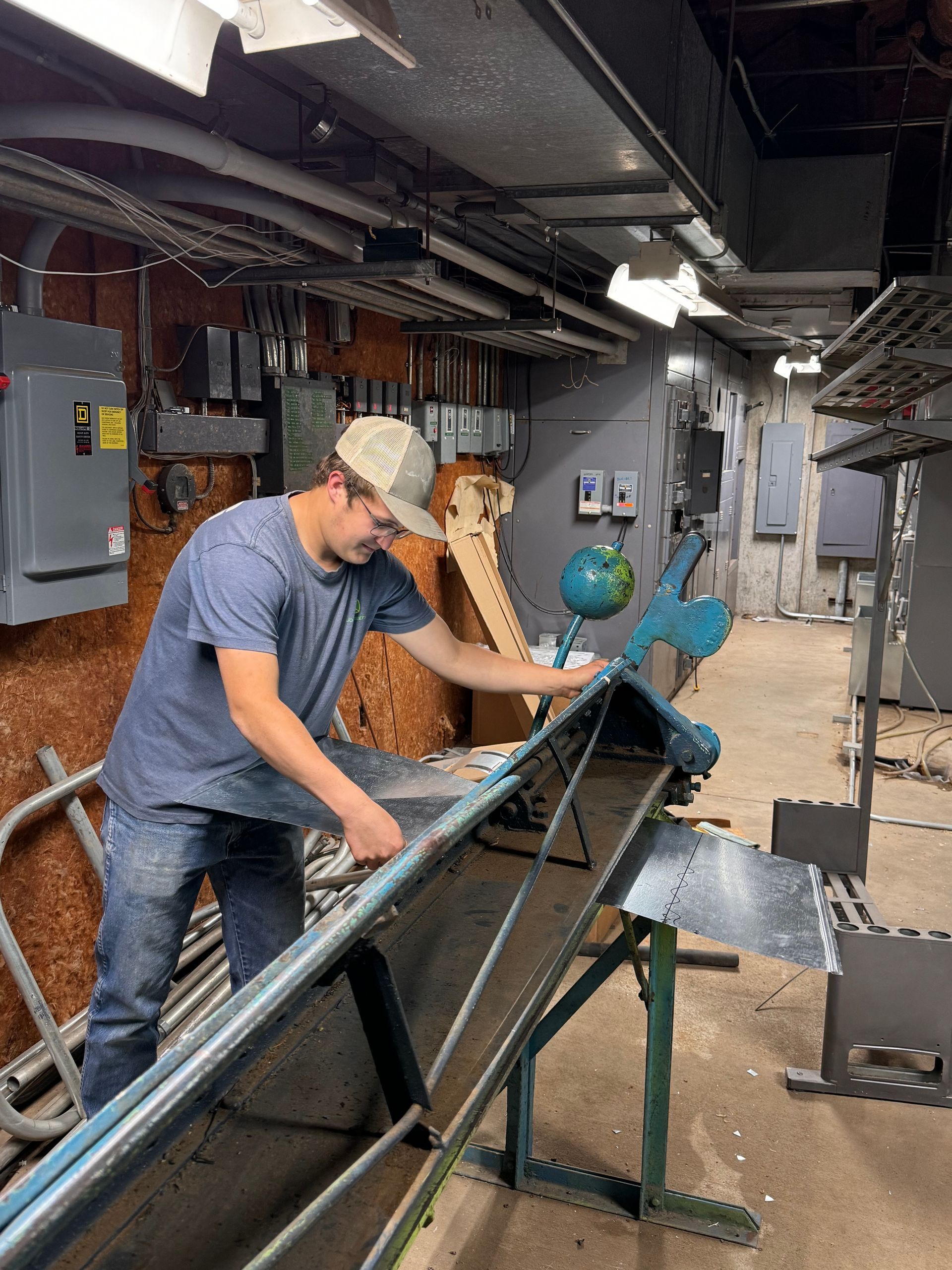 Worker operating a metal-cutting machine in an industrial workshop, with long steel beams on a stand.