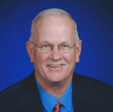 Portrait of a smiling man in glasses, wearing a blue shirt and dark jacket against a blue background