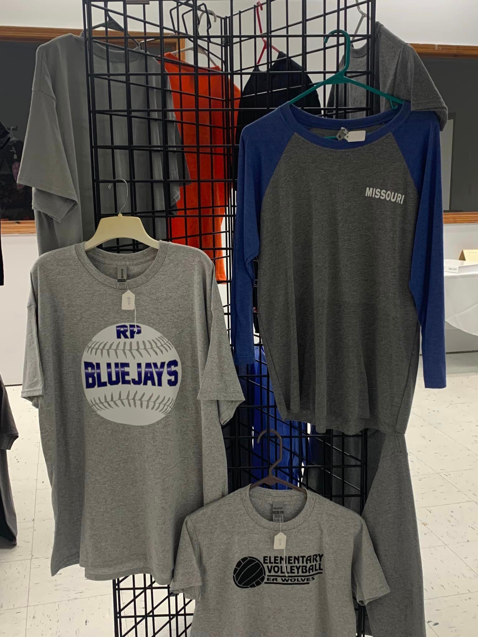 Gray and navy long-sleeve shirts with Blue Jays graphics hanging on a store display rack