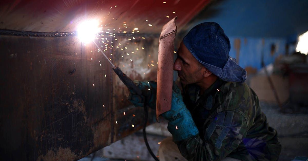 Worker welding metal in a dim workshop, sparks flying from the torch.