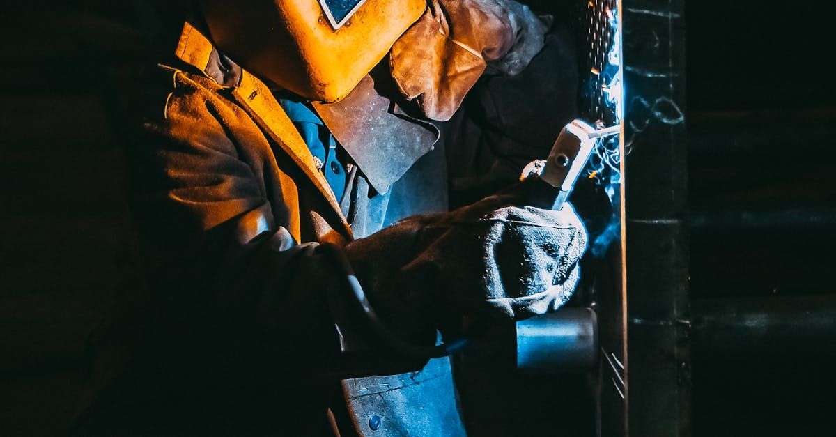 Worker in orange safety jacket handling metal equipment in a dark industrial setting