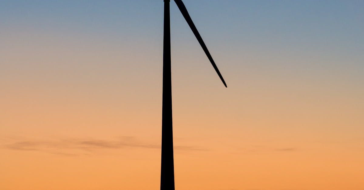 Silhouette of a wind turbine against an orange sunset sky