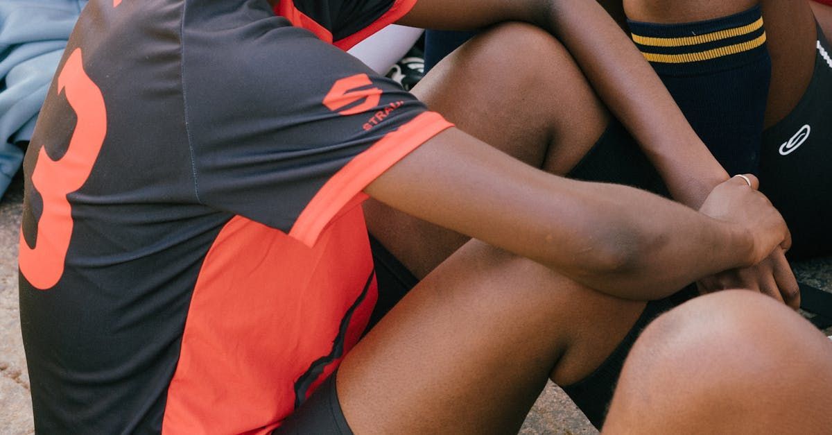 People in black and red sports uniforms sitting closely together on grass or a field