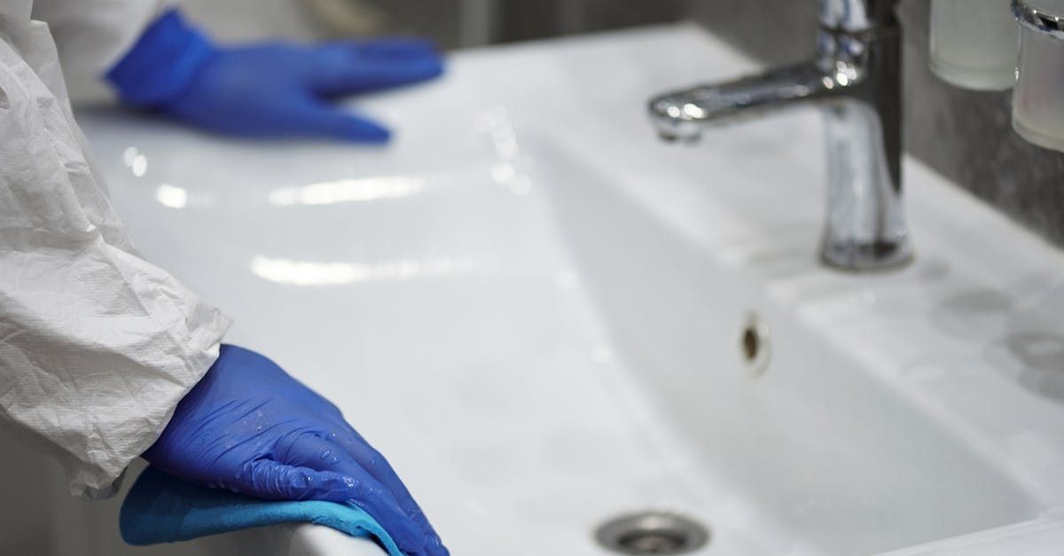 Blue-gloved hands at a white sink in a clinical setting