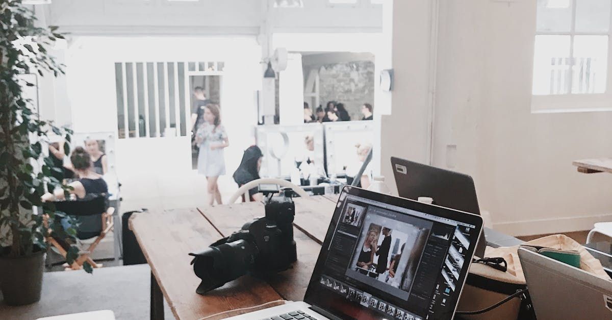 Bright home office with a laptop, camera gear on a table, and a person in the background near a doorway