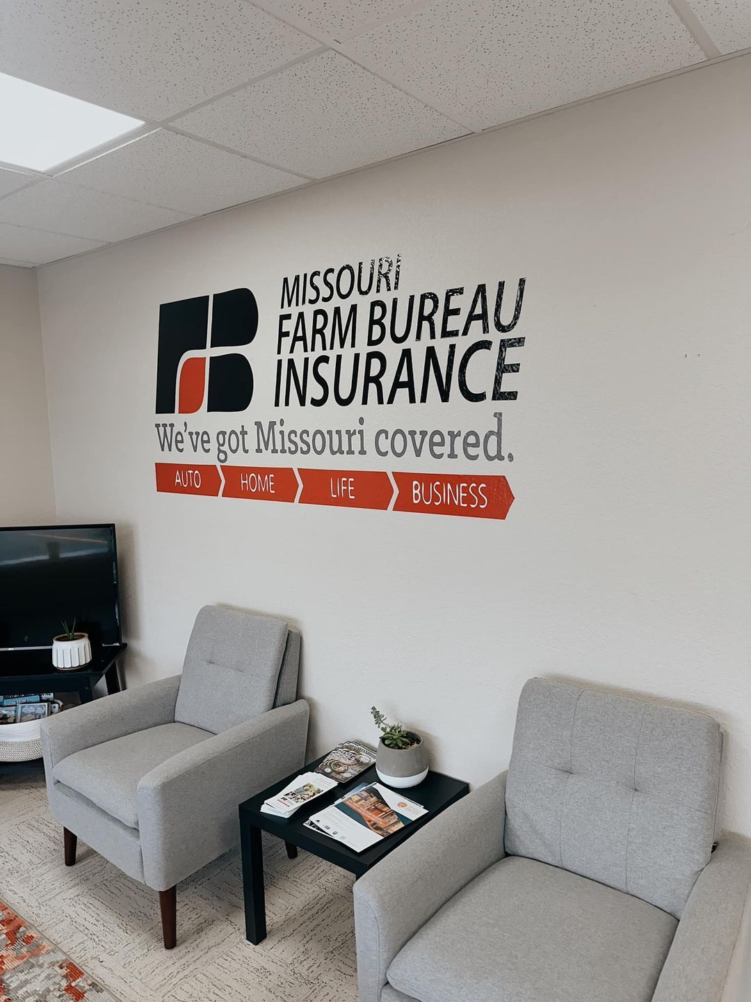 Office waiting area with Missouri Farm Bureau Insurance wall sign, two gray chairs, and a small table