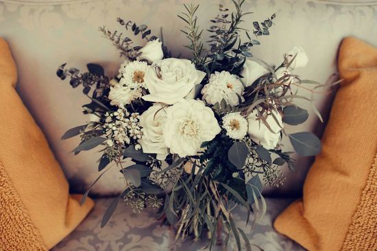 A bouquet of white flowers is sitting on a couch next to two pillows.