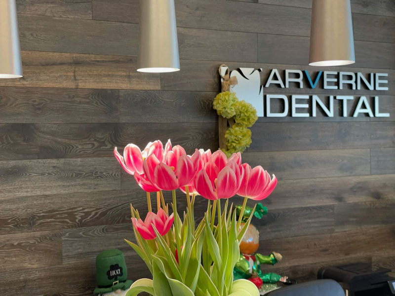 Pink tulips in vase on dental office reception desk, with “Tarverne Dental” sign in background.