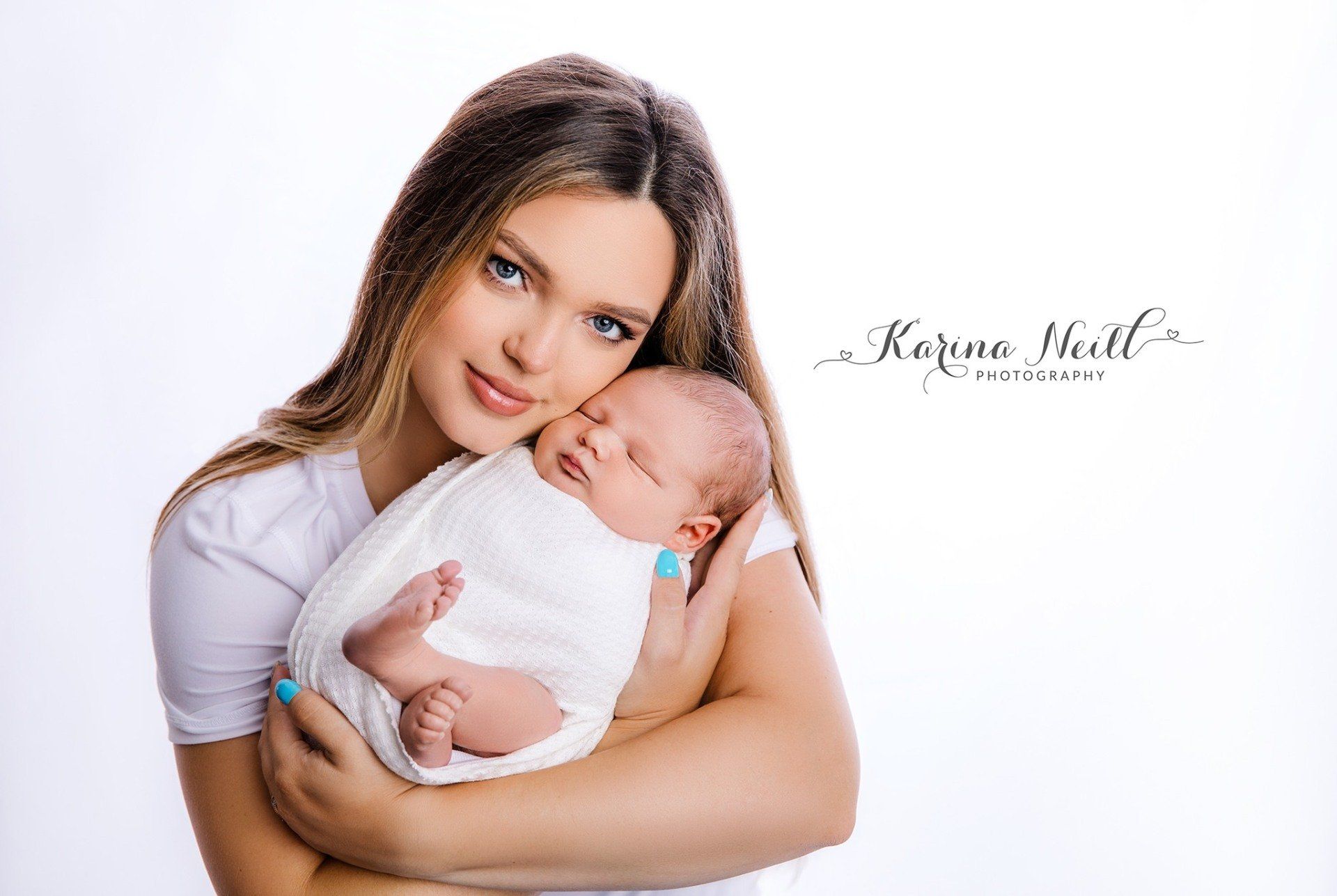 A woman is holding a newborn baby wrapped in a white blanket.