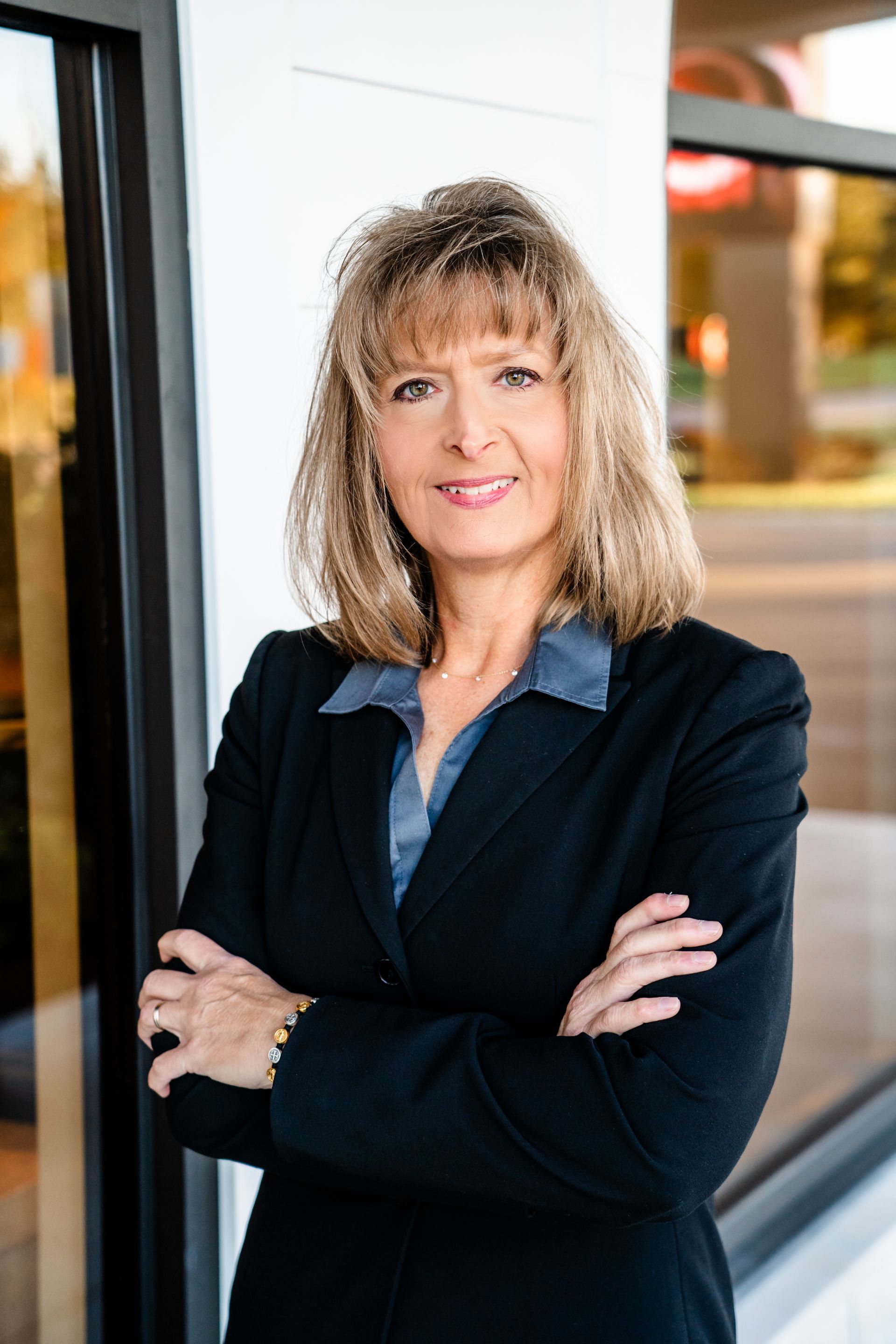A woman in a suit is standing with her arms crossed in front of a building.