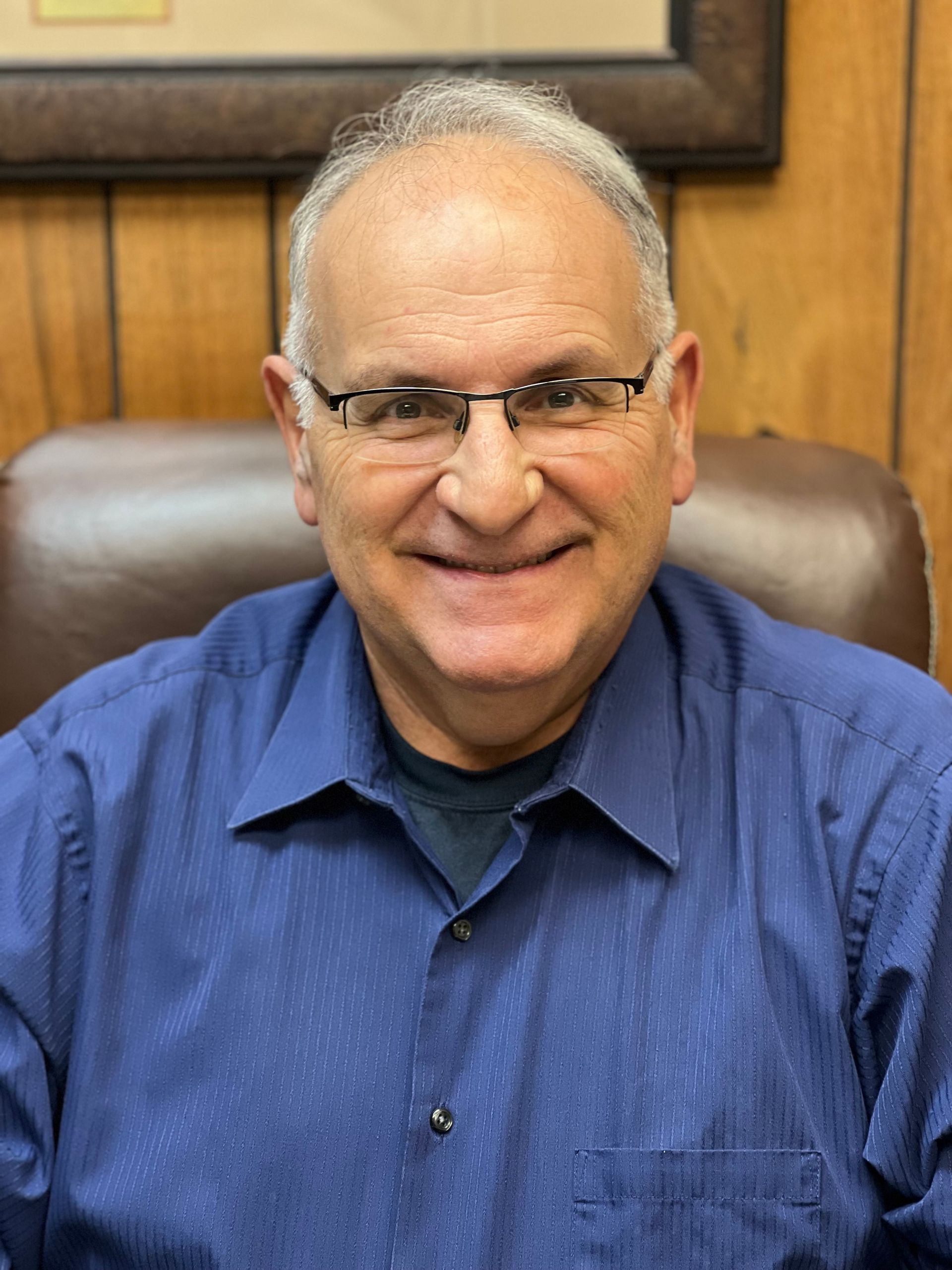 A man wearing glasses and a blue shirt is sitting in a chair.