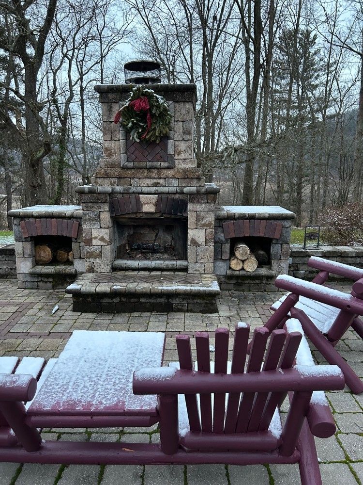 A brick fireplace with a wreath on top of it is surrounded by purple chairs.