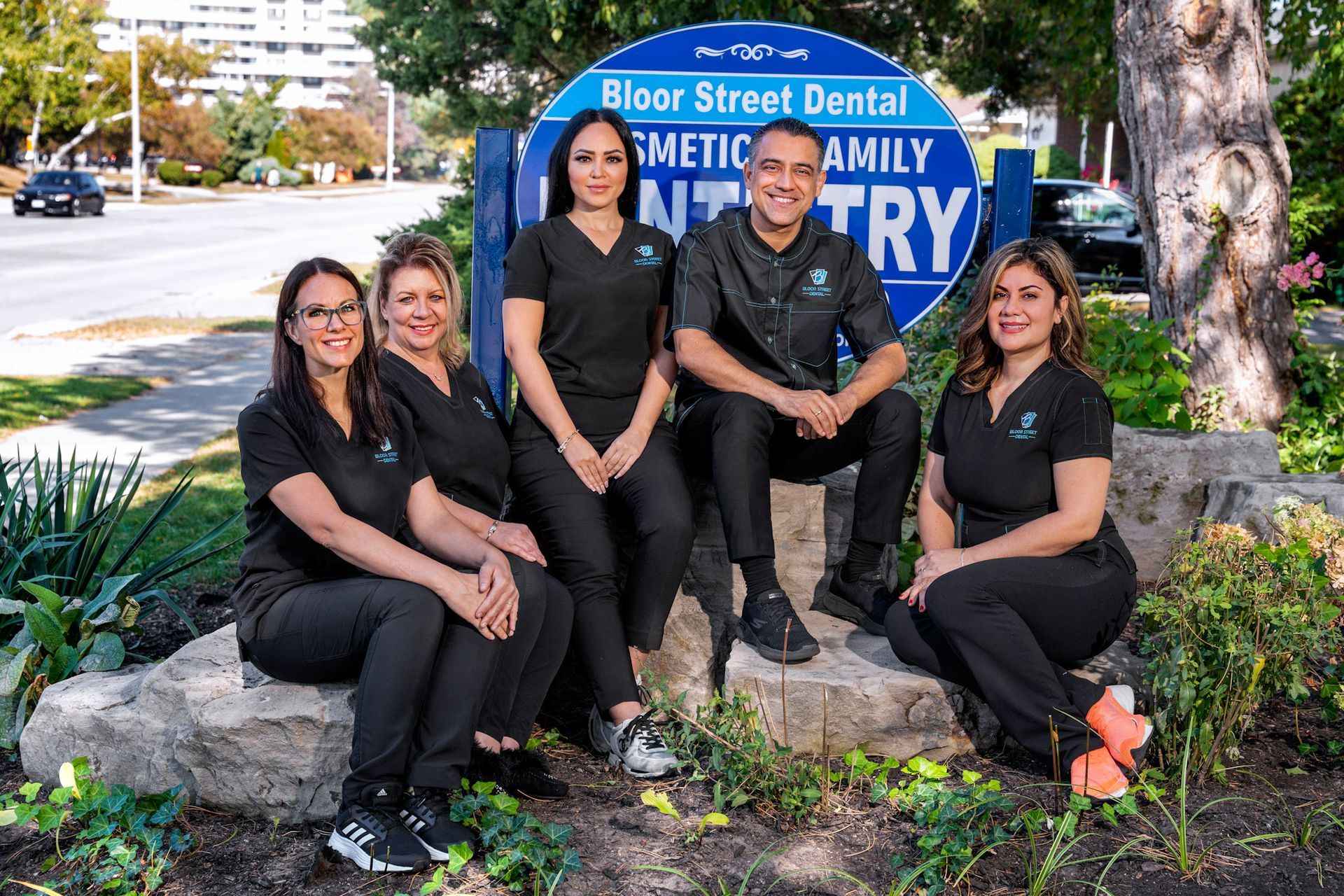 a dental team posing in front of a bloor street dental sign | Bloor Street Dental | Best Family and Cosmetic Dentist In Mississauga For Implants, Braces, and Invisalign
