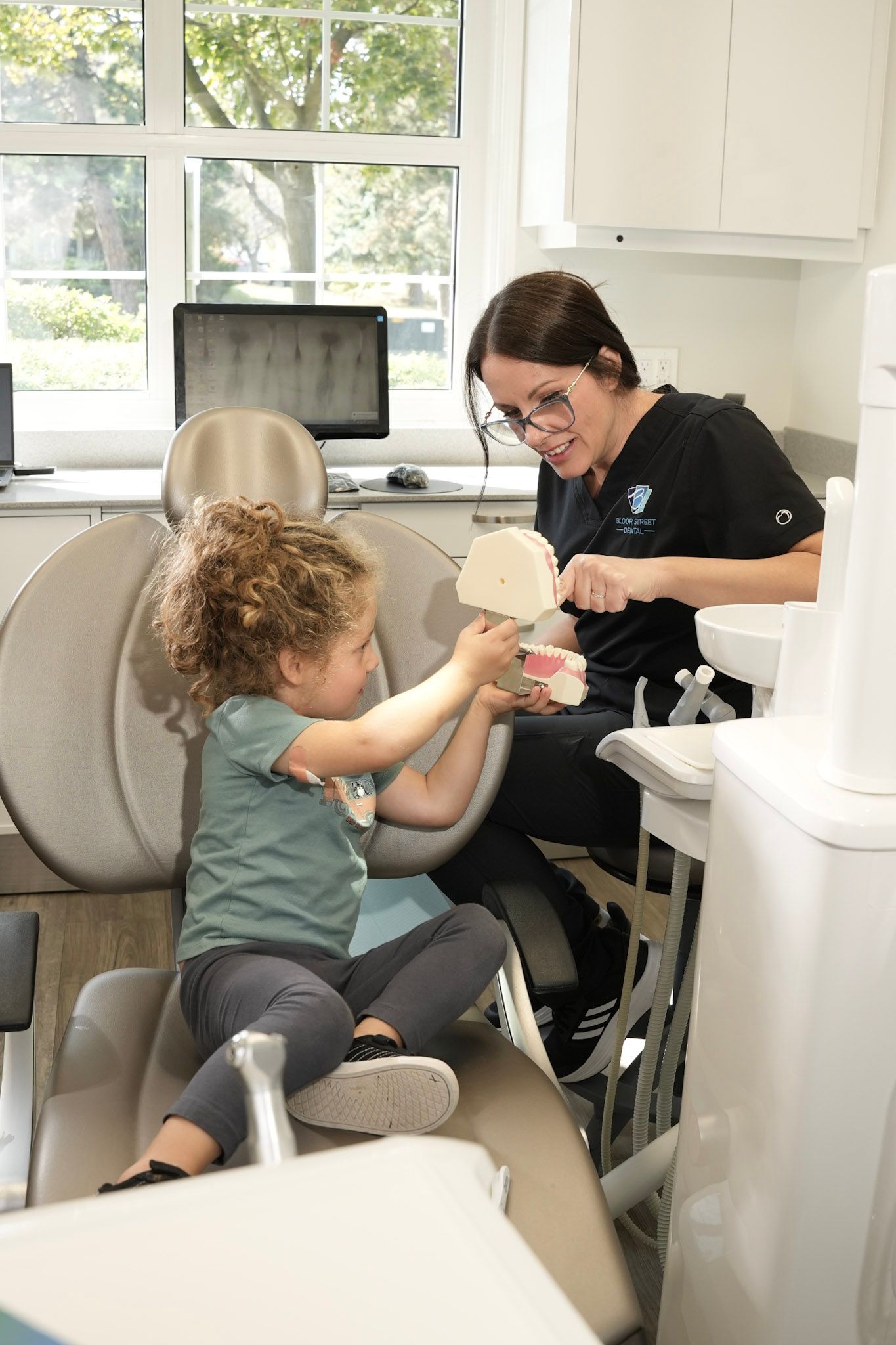 a little boy sitting in a dental chair looking at a model of teeth | Bloor Street Dental | Best Family and Cosmetic Dentist In Mississauga For Implants, Braces, and Invisalign