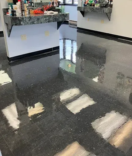 Black speckled floor in a salon with white patches and reflective surfaces. Counters with products are in the background.