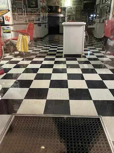 Black and white checkered floor in an interior, leading to a counter. Red chairs, display cases, and framed photos fill the room.